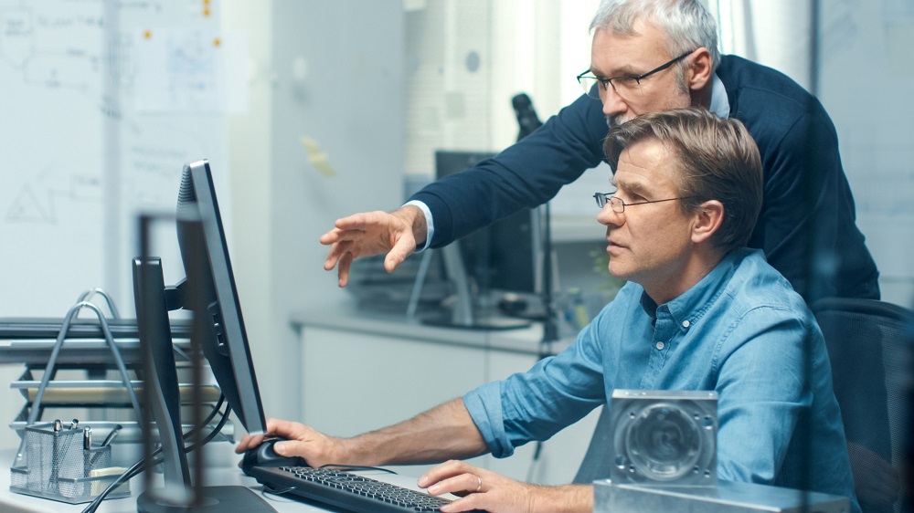 Two professionals consult in front of a computer screen.