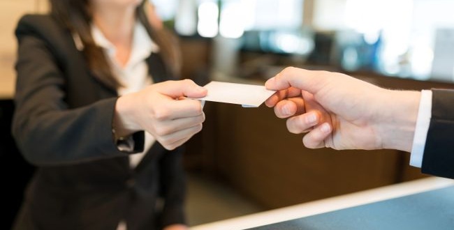 A kép illusztráció, melyen két ember a recepciós pultnál borítékot cserél.