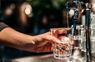 A kép illusztráció, melyen egy bárpultra szerelt vízcsapból vizet töltenek egy pohárba.