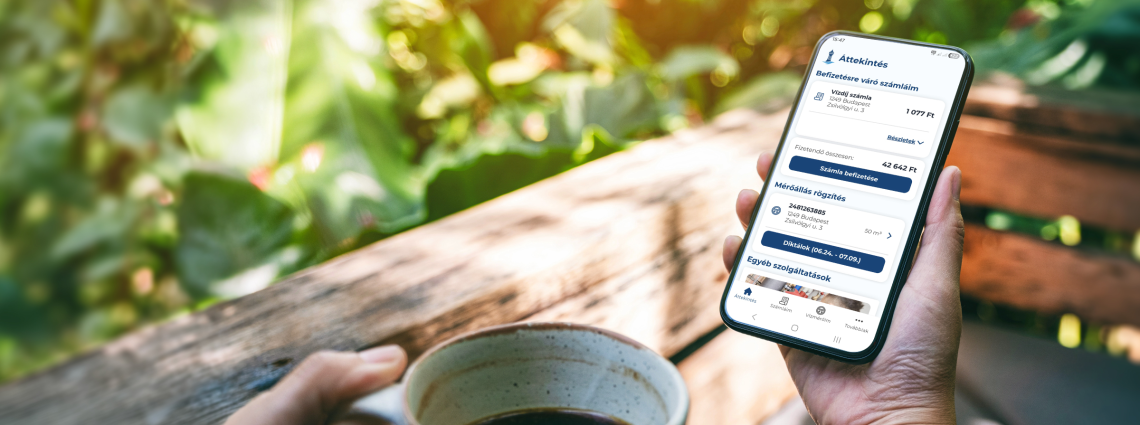 A képen egy mobiltelefont tartó ember keze látható, aki az applikációban éppen ügyintéz, miközben kirándul.
